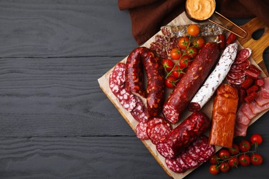 Photo of Different types of delicious sausages, sauce and tomatoes on black wooden table, flat lay. Space for text