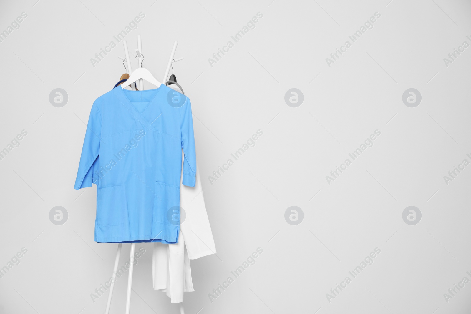 Photo of Medical uniforms hanging on rack against light grey background. Space for text