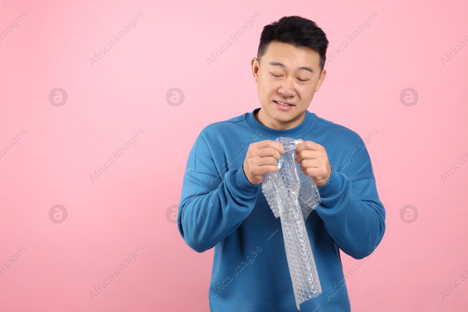 Photo of Asian man with bubble wrap on pink background. Space for text