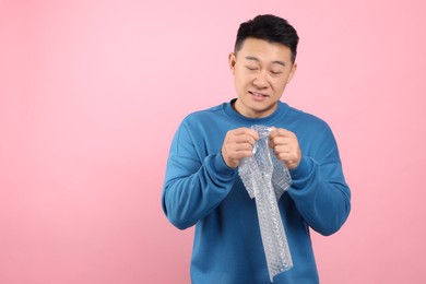 Asian man with bubble wrap on pink background. Space for text