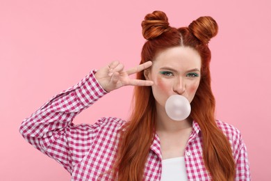 Photo of Beautiful woman with bright makeup blowing bubble gum and gesturing on pink background