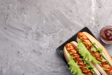 Photo of Tasty hot dogs with lettuce, ketchup and mustard on grey textured table, flat lay. Space for text