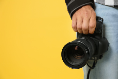 Photo of Professional photographer with modern camera on yellow background in studio, closeup. Space for text