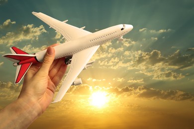 Image of Woman holding model of airplane against beautiful sky at sunset, closeup. Travel concept
