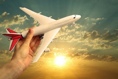 Woman holding model of airplane against beautiful sky at sunset, closeup. Travel concept