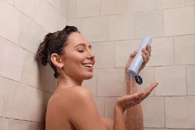 Photo of Happy woman pouring shampoo in shower at home. Washing hair