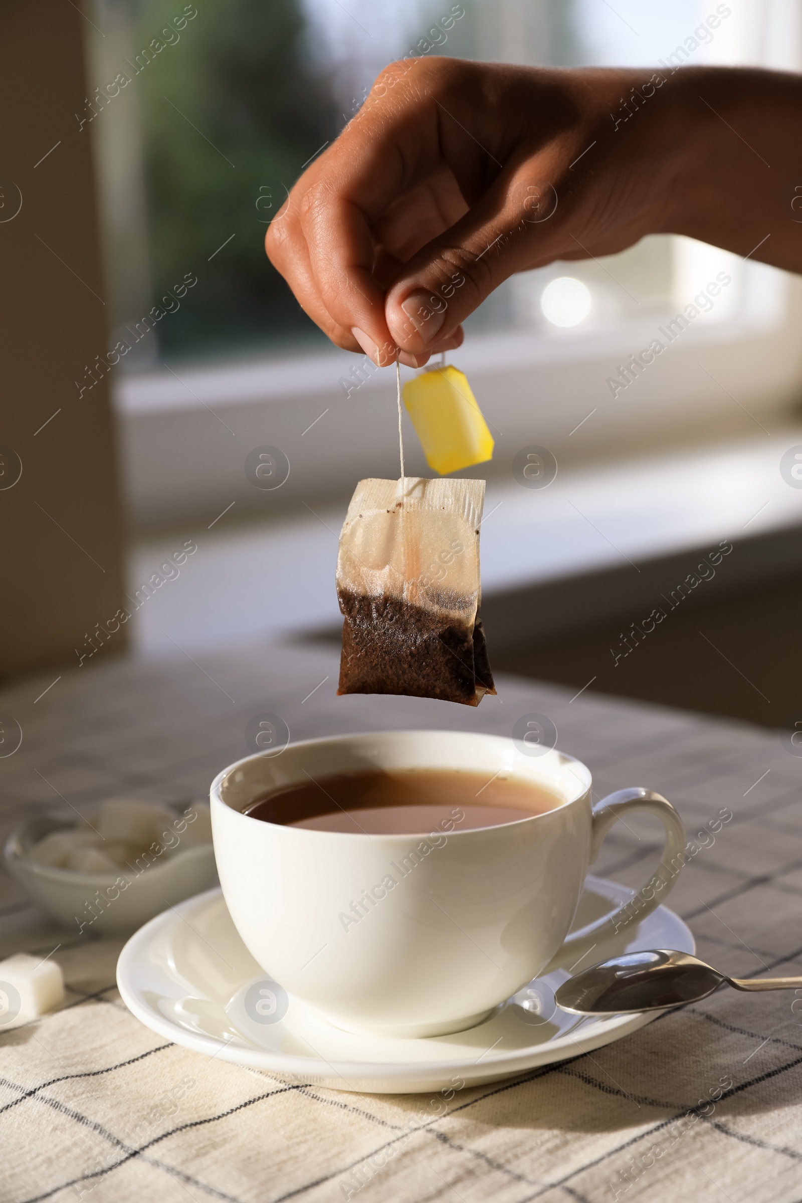 Photo of Woman taking tea bag out of cup at table indoors, closeup