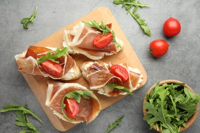 Photo of Tasty sandwiches with cured ham, tomatoes and arugula on grey table, flat lay