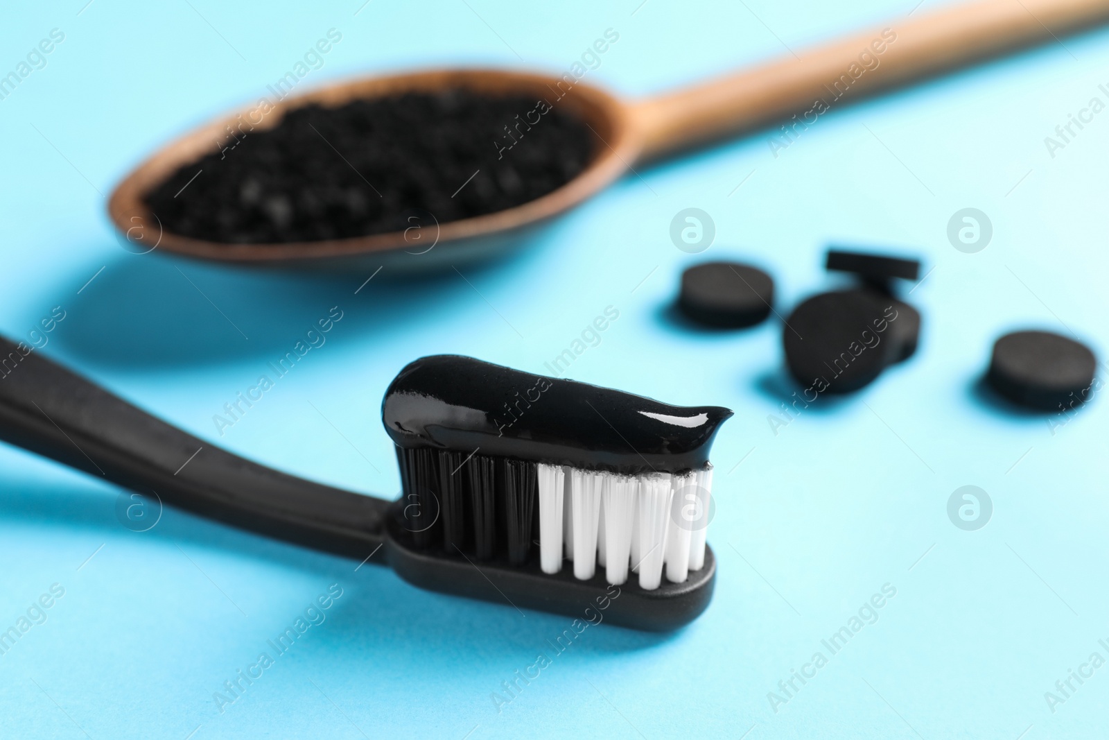 Photo of Brush with charcoal toothpaste on light blue background, closeup