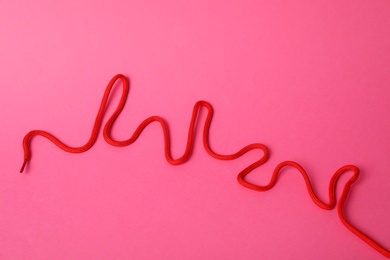 Photo of Red shoe lace on pink background, top view