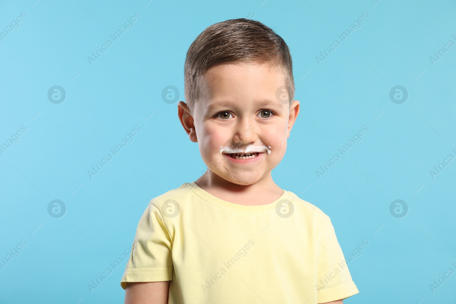 Photo of Cute boy with milk mustache on light blue background