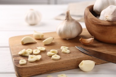 Aromatic cut garlic, cloves and bulbs on white wooden table, closeup