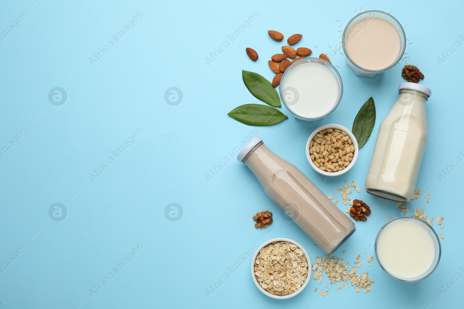 Photo of Different vegan milks and ingredients on light blue background, flat lay. Space for text