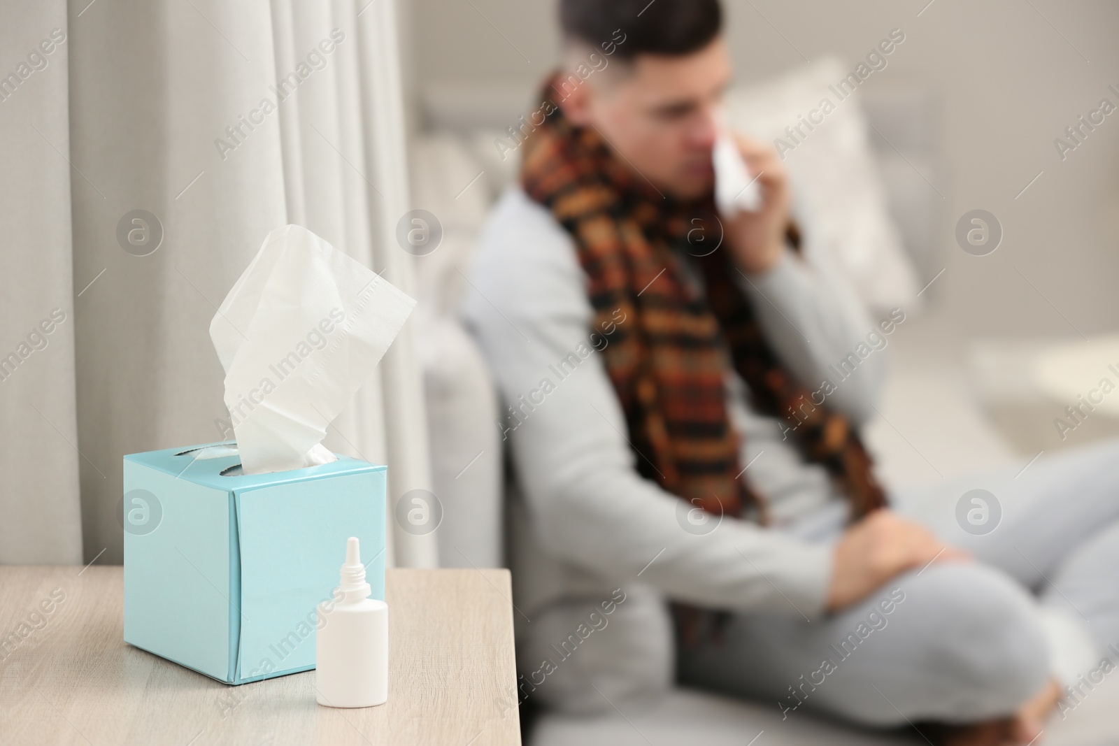 Photo of Ill man at home, focus on nasal spray and box of tissues 
