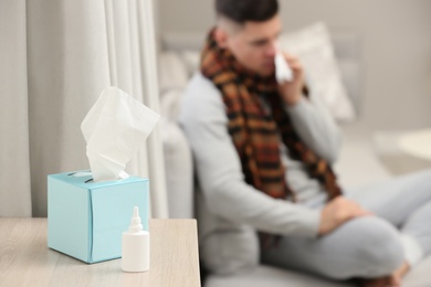 Photo of Ill man at home, focus on nasal spray and box of tissues 