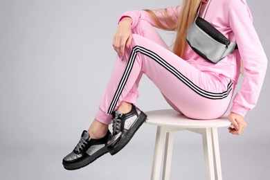 Photo of Woman in stylish sport shoes with bum bag sitting on stool against light background