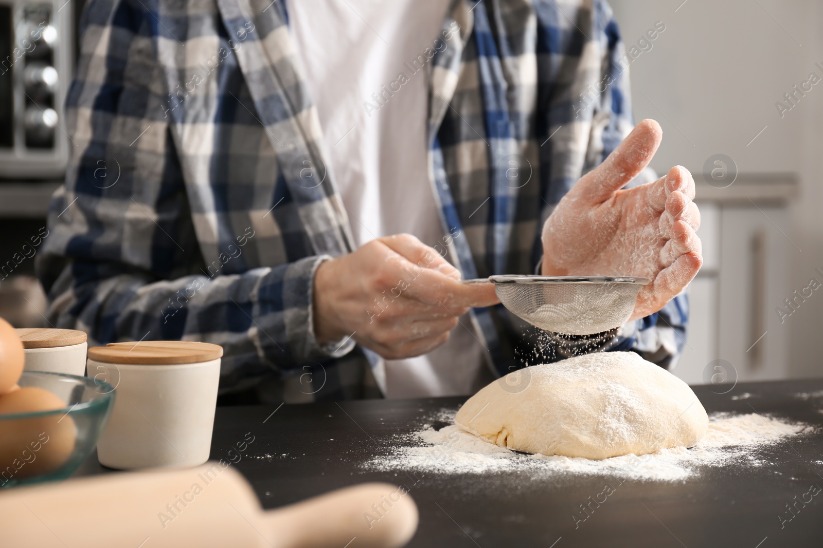 Photo of Man sprinkling flour over dough on table in kitchen