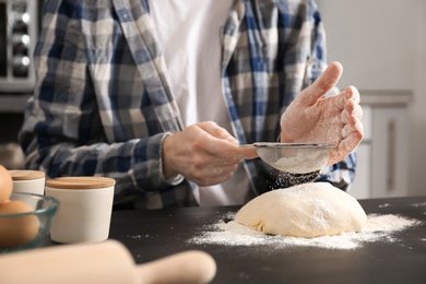 Man sprinkling flour over dough on table in kitchen