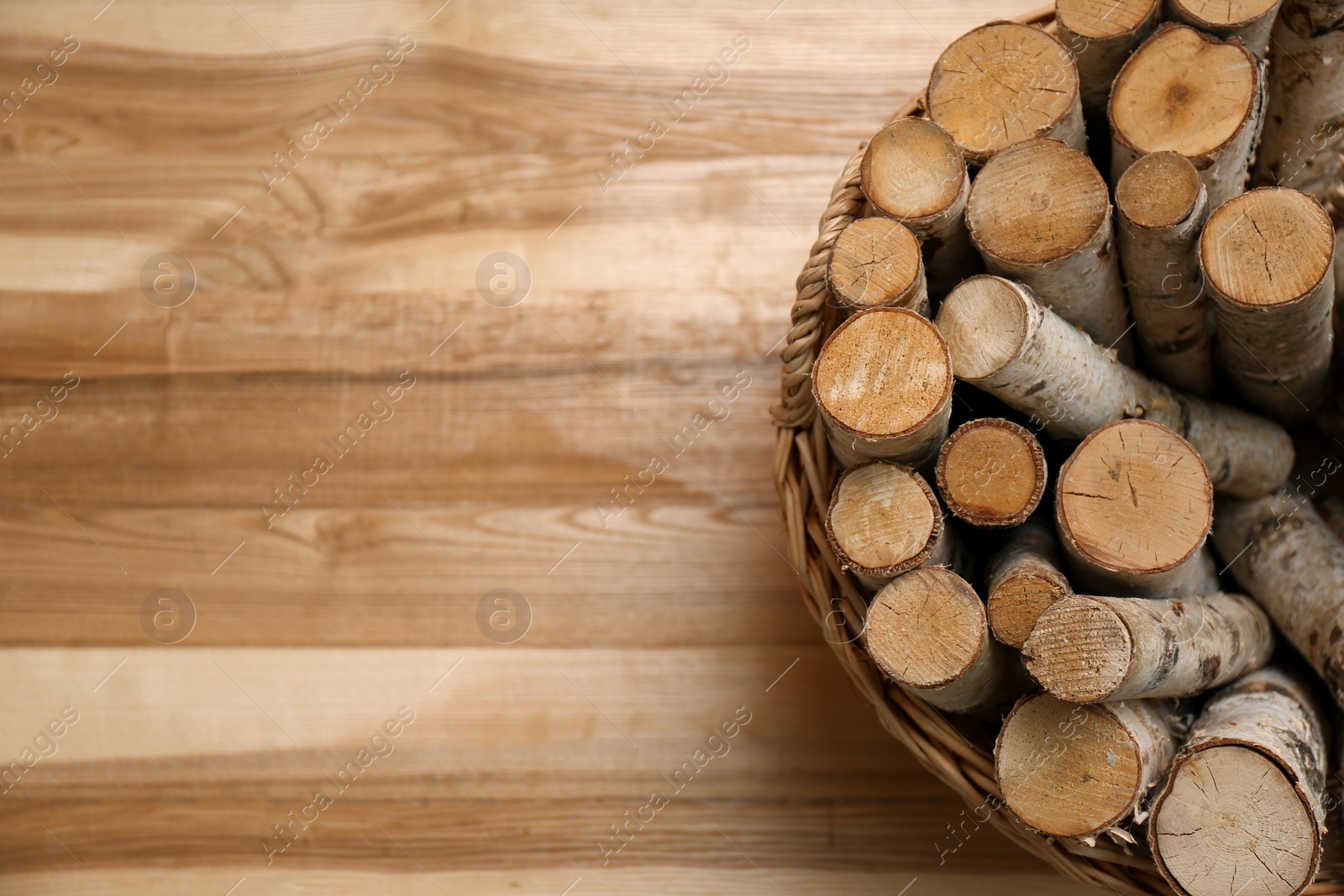Photo of Wicker basket with firewood on floor indoors, top view. Space for text