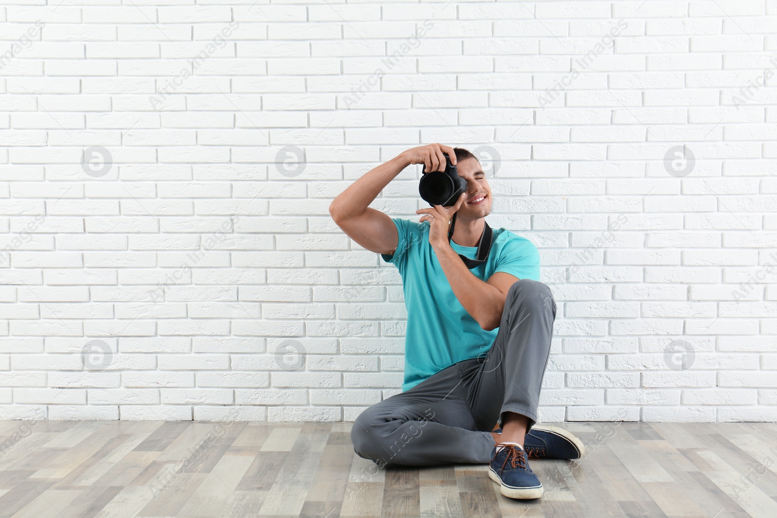 Photo of Young professional photographer taking picture near brick wall. Space for text