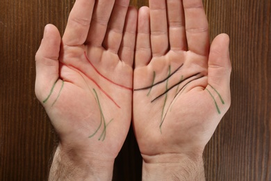 Photo of Man showing palms with drawn lines on wooden background, top view. Chiromancy and foretelling