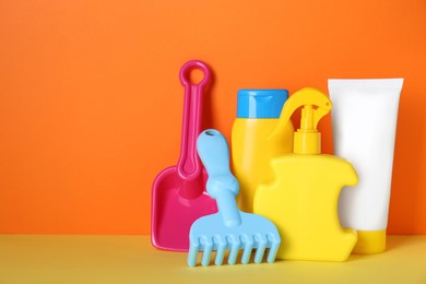 Different suntan products and plastic beach toys on color background. Space for text
