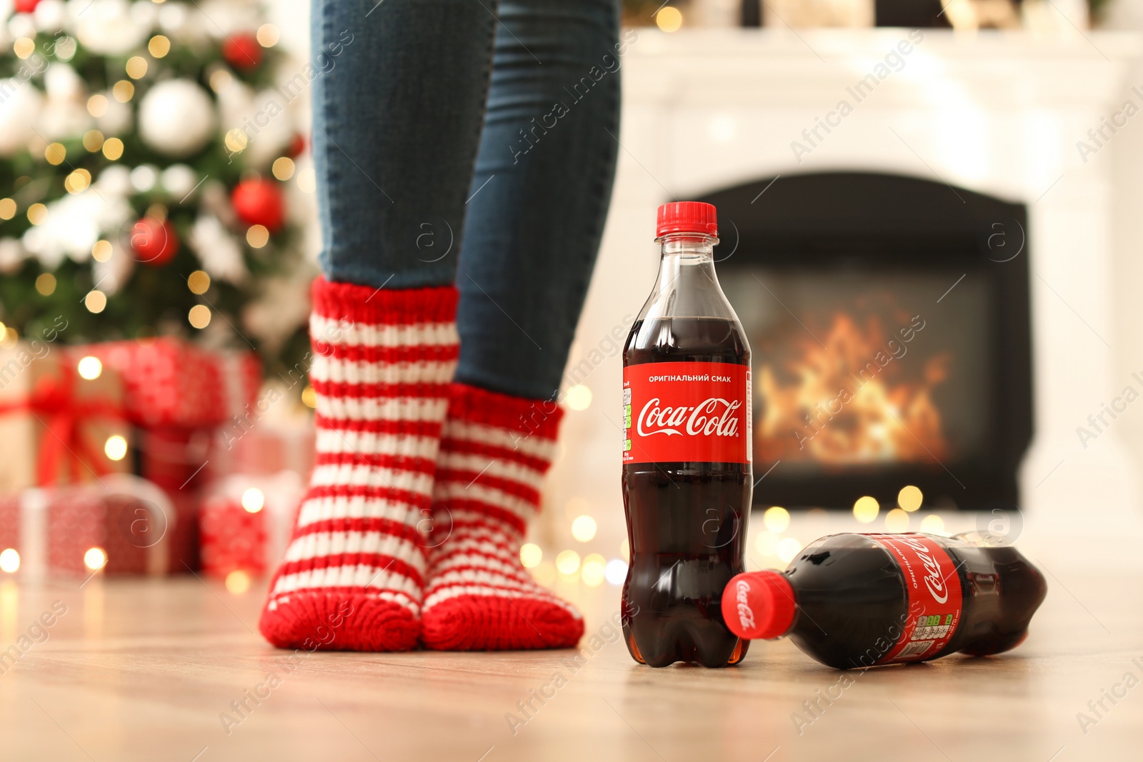 Photo of MYKOLAIV, UKRAINE - JANUARY 15, 2021: Woman near Coca-Cola bottles in room decorated for Christmas, closeup