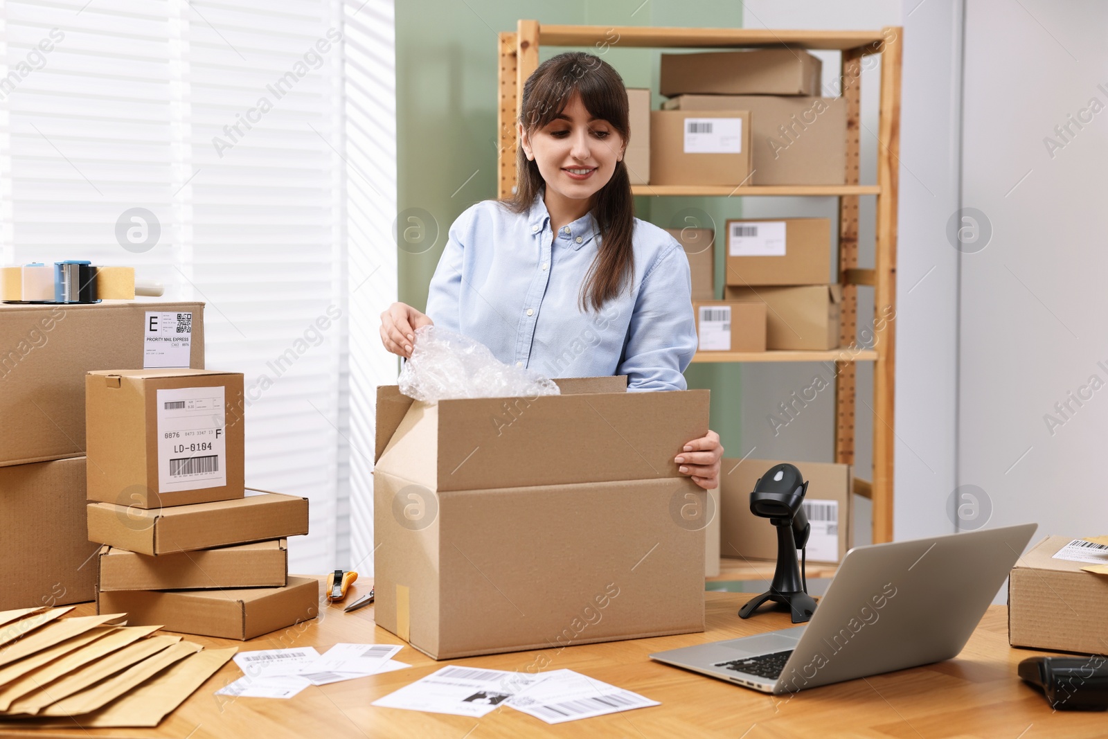 Photo of Post office worker packing parcel at wooden table indoors