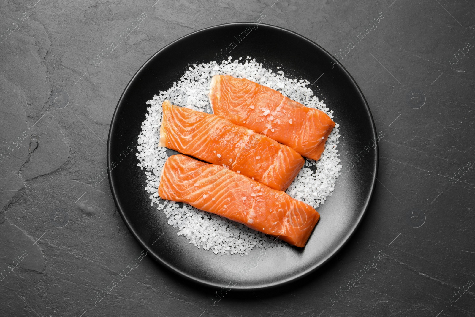 Photo of Fresh raw salmon with salt on black table, top view