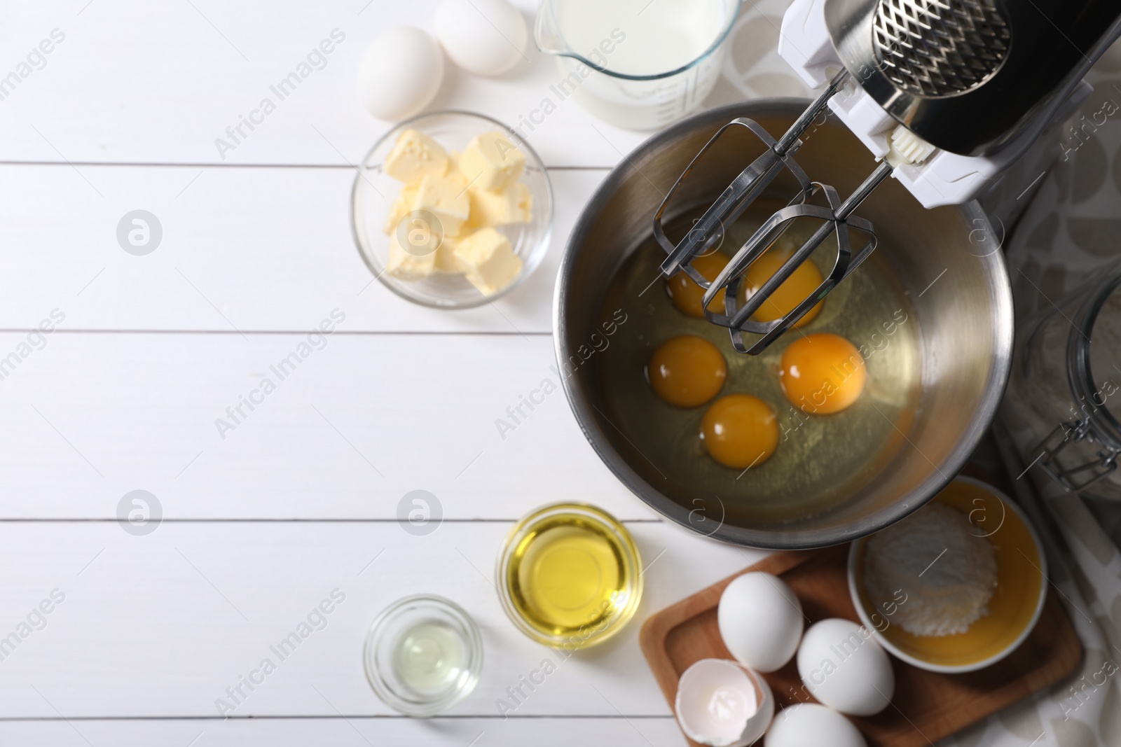 Photo of Making dough. Raw eggs in bowl of stand mixer and ingredients on white wooden table, flat lay with space for text