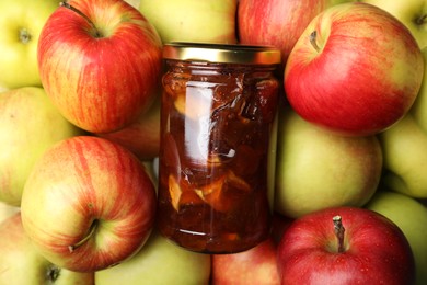 Photo of Delicious apple jam in jar on fresh fruits, top view