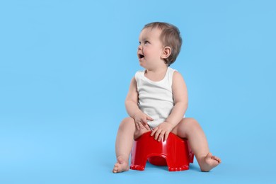 Photo of Little child sitting on baby potty against light blue background. Space for text