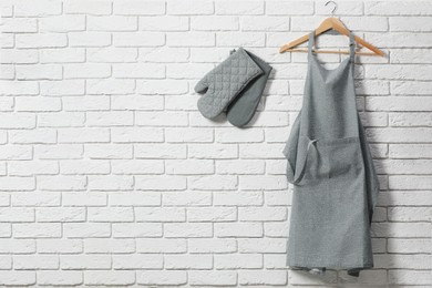 Photo of Clean kitchen apron with pattern and oven gloves on white brick wall. Space for text
