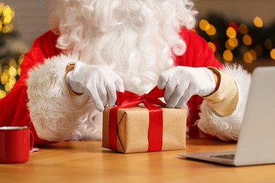 Photo of Santa Claus decorating Christmas gift with ribbon at home, closeup