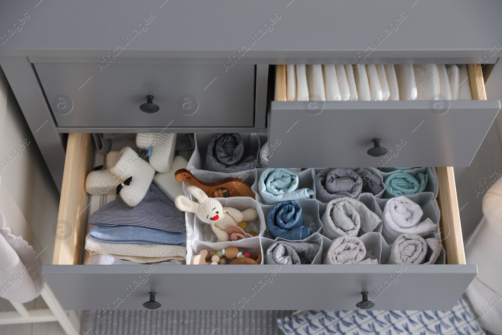 Photo of Modern open chest of drawers with clothes and accessories in baby room, above view