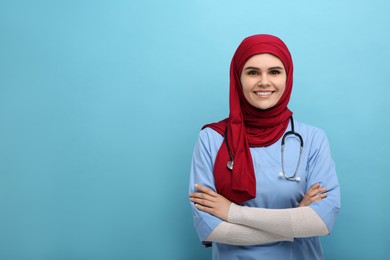 Muslim woman wearing hijab and medical uniform with stethoscope on light blue background, space for text