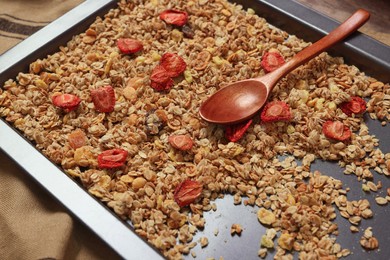 Making granola. Baking tray with mixture of oat flakes, other ingredients and spoon on table