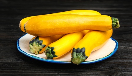 Plate with fresh ripe yellow zucchini on black wooden table