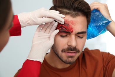 Photo of Nurse examining young man's head injury in clinic. First aid