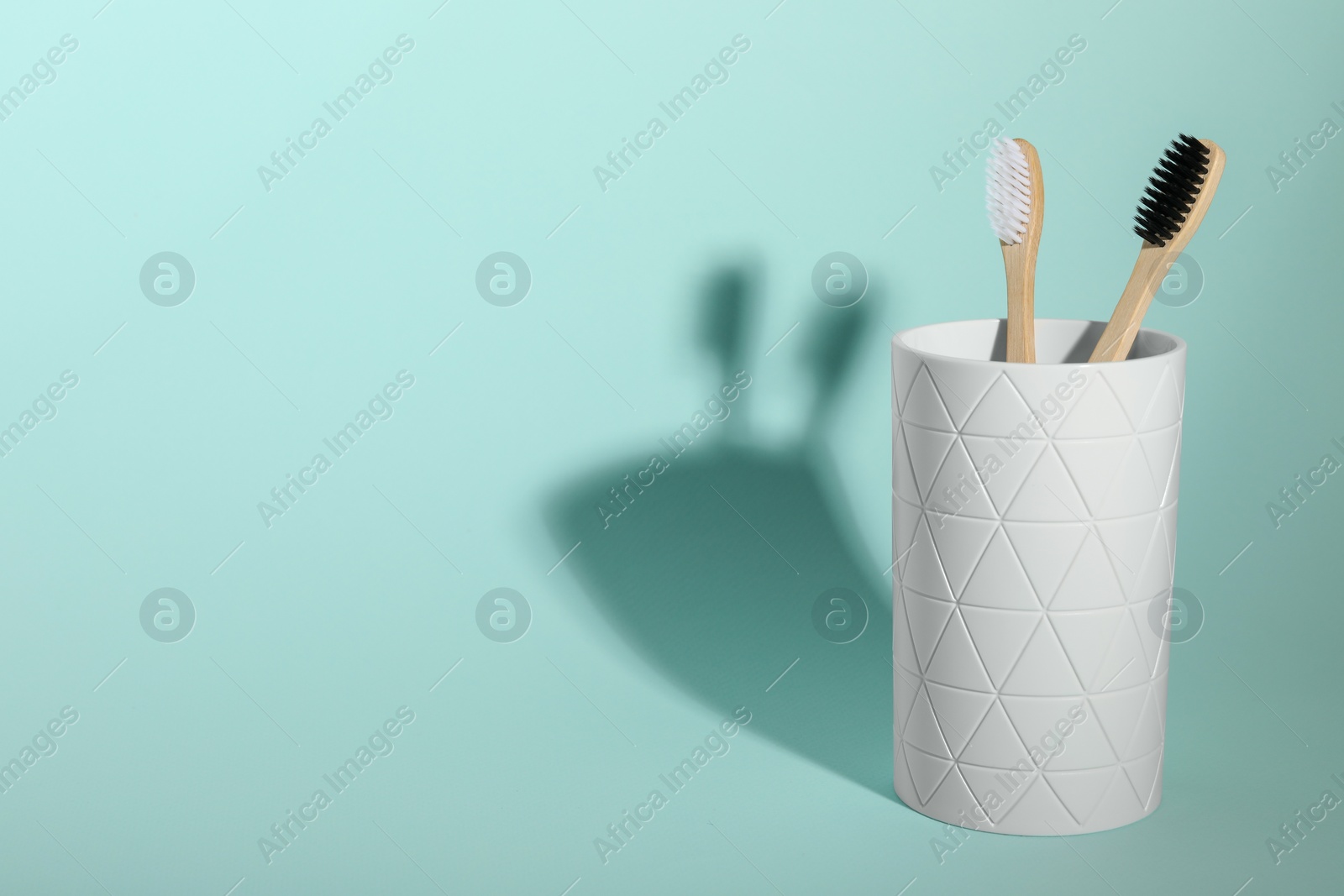 Photo of Bamboo toothbrushes in holder on turquoise background, space for text