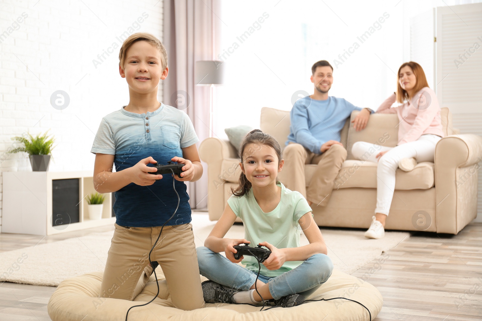 Photo of Cute children playing video games while parents resting on sofa at home