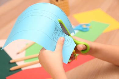 Photo of Little boy cutting color paper with scissors at table indoors, closeup