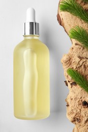 Bottle of hydrophilic oil near tree bark with fir twigs on white background, flat lay