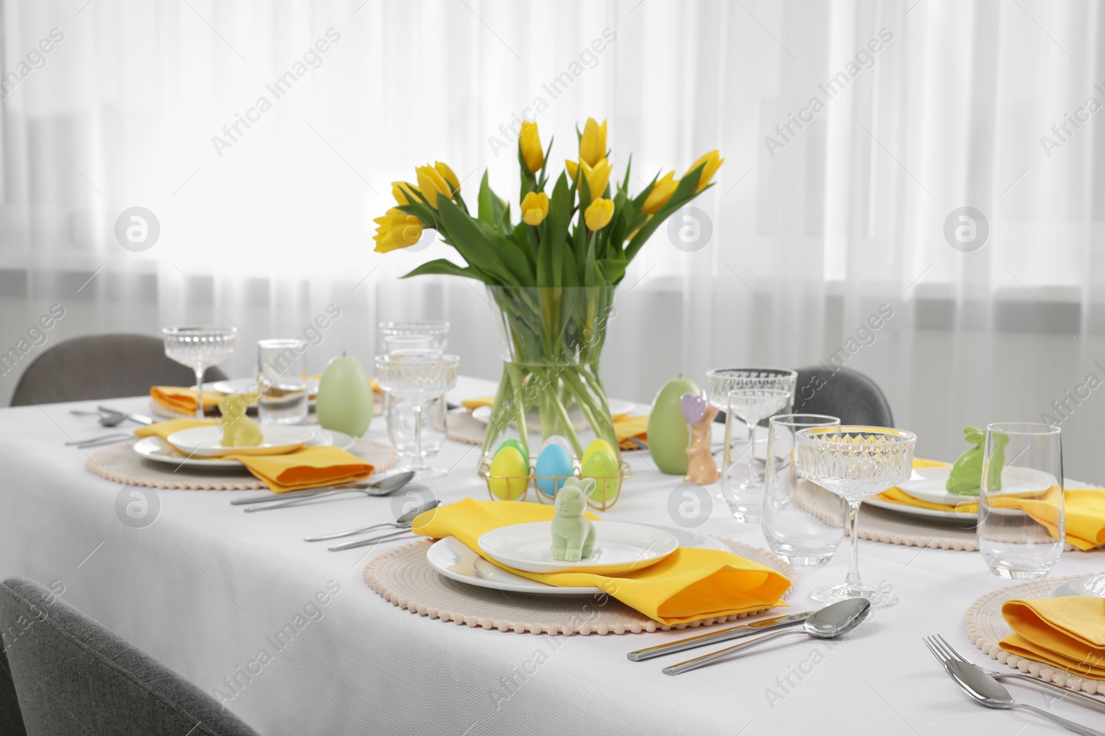 Photo of Festive table setting with glasses, painted eggs and vase of tulips. Easter celebration