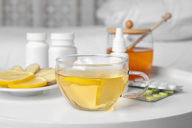 Glass cup of hot tea with lemon and different cold remedies on white table