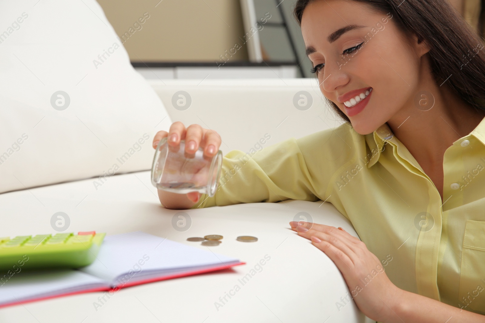 Photo of Young woman counting money near sofa at home