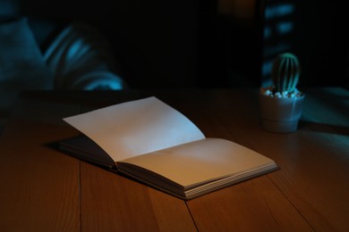 Photo of Open book on wooden table at night