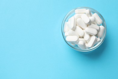 Photo of Vitamin capsules in bowl on light blue background, top view. Space for text