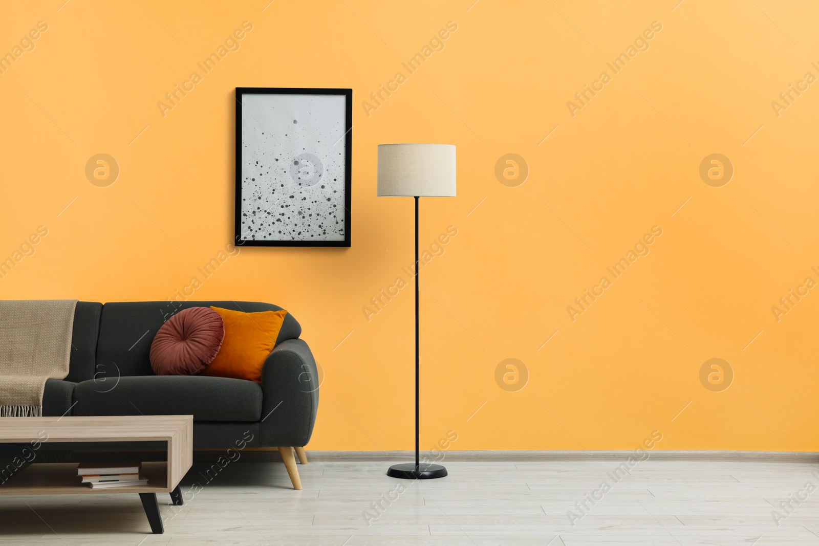 Photo of Stylish grey sofa with colorful pillows, wooden table and lamp near pale orange wall indoors. Interior design