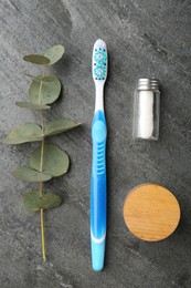 Plastic toothbrush, eucalyptus branch and other toiletries on grey table, flat lay